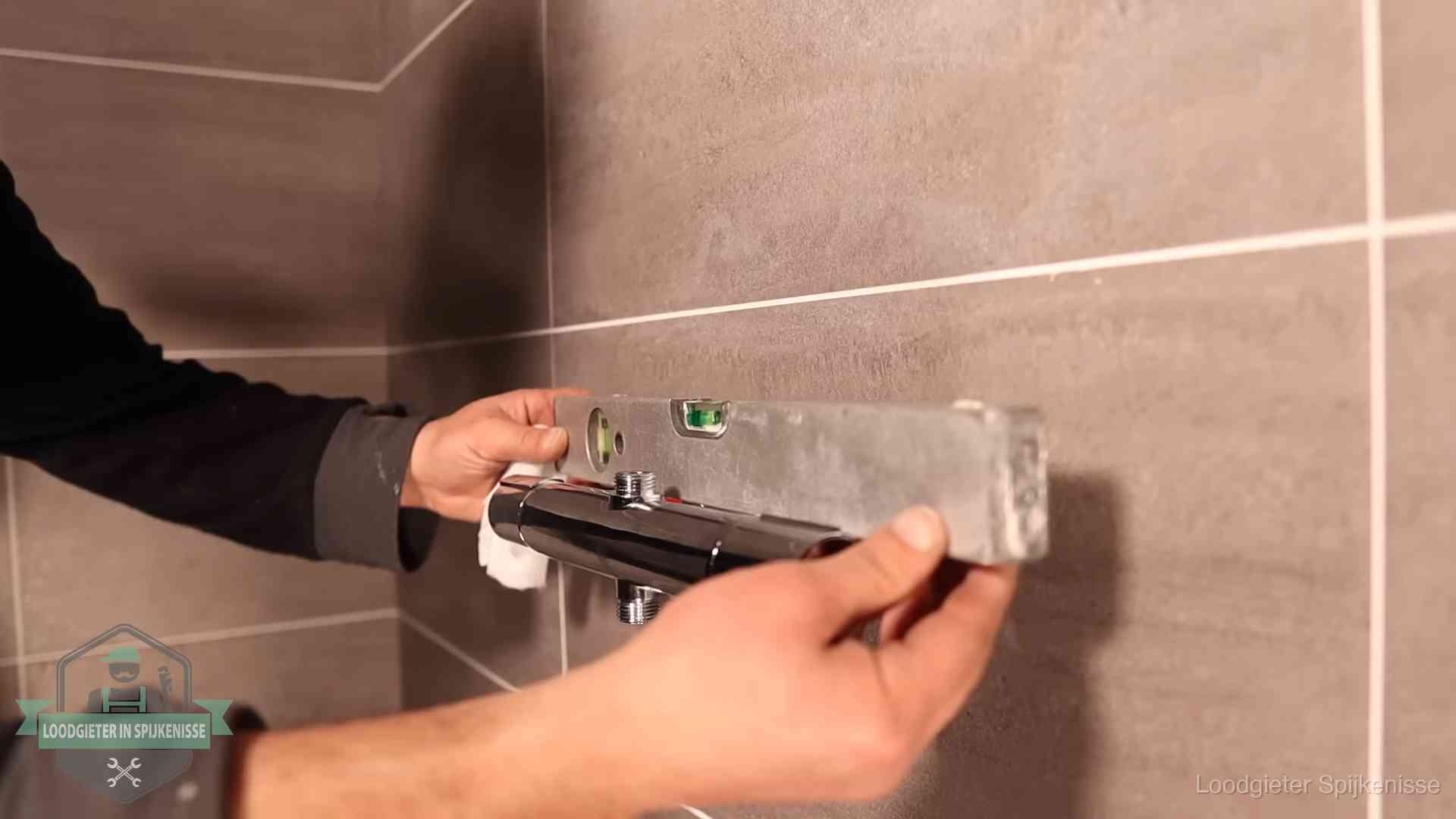 Loodgieter lijnt een douchekraan uit met een waterpas in een woning in Spijkenisse